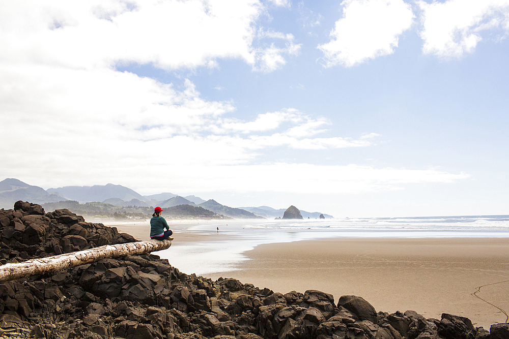 Caucasian woman sitting on log on rocks at beach