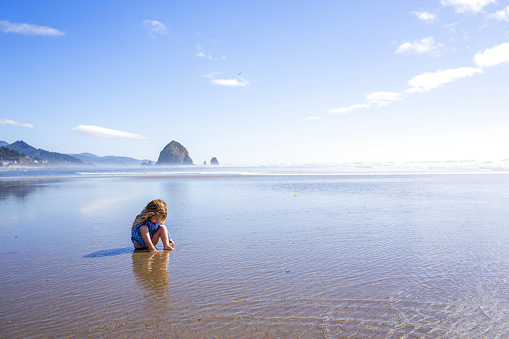 Caucasian girl sitting on beach in ocean waves