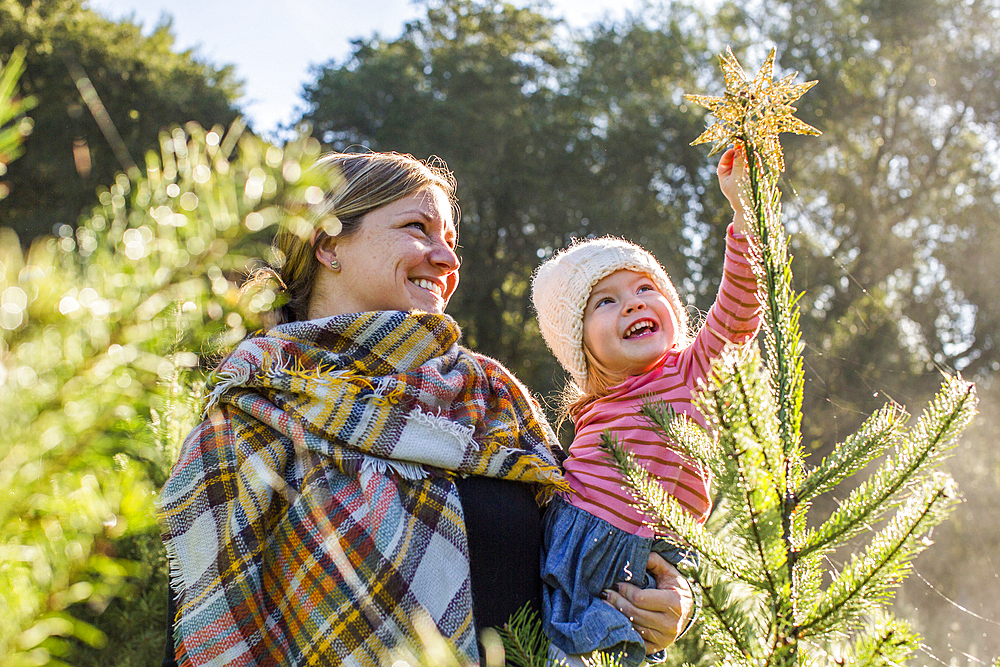 Caucasian mother helping daughter place star on top of Christmas tree