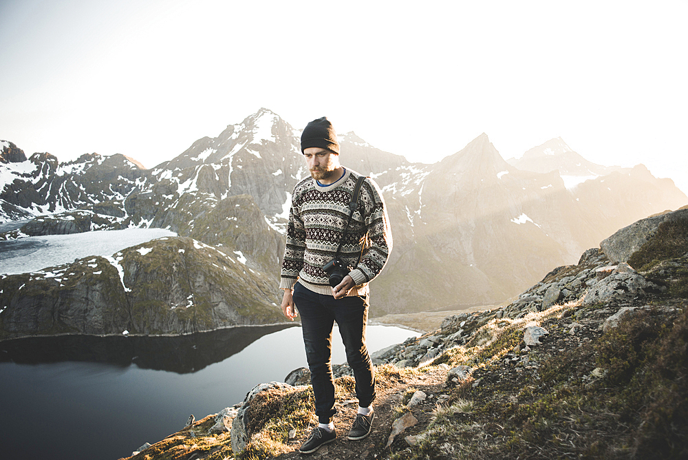 Caucasian man carrying camera near mountain lake