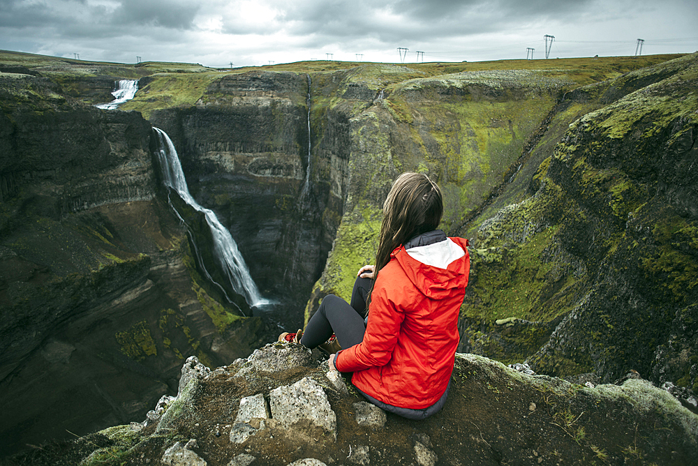 Caucasian woman sitting on cliff admiring waterfall