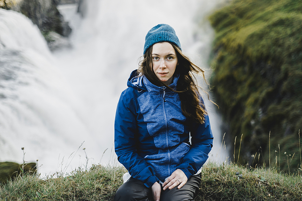 Portrait of serious Caucasian woman sitting near waterfall