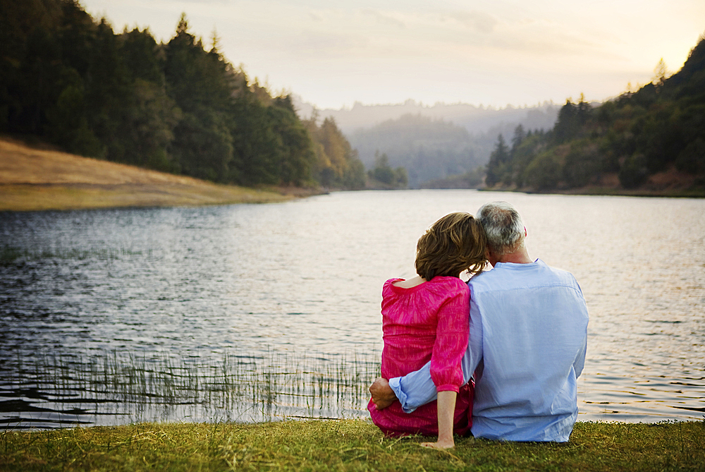 Couple sitting in grass and hugging near river