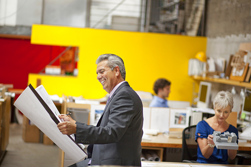 Smiling architect reading blueprint in office