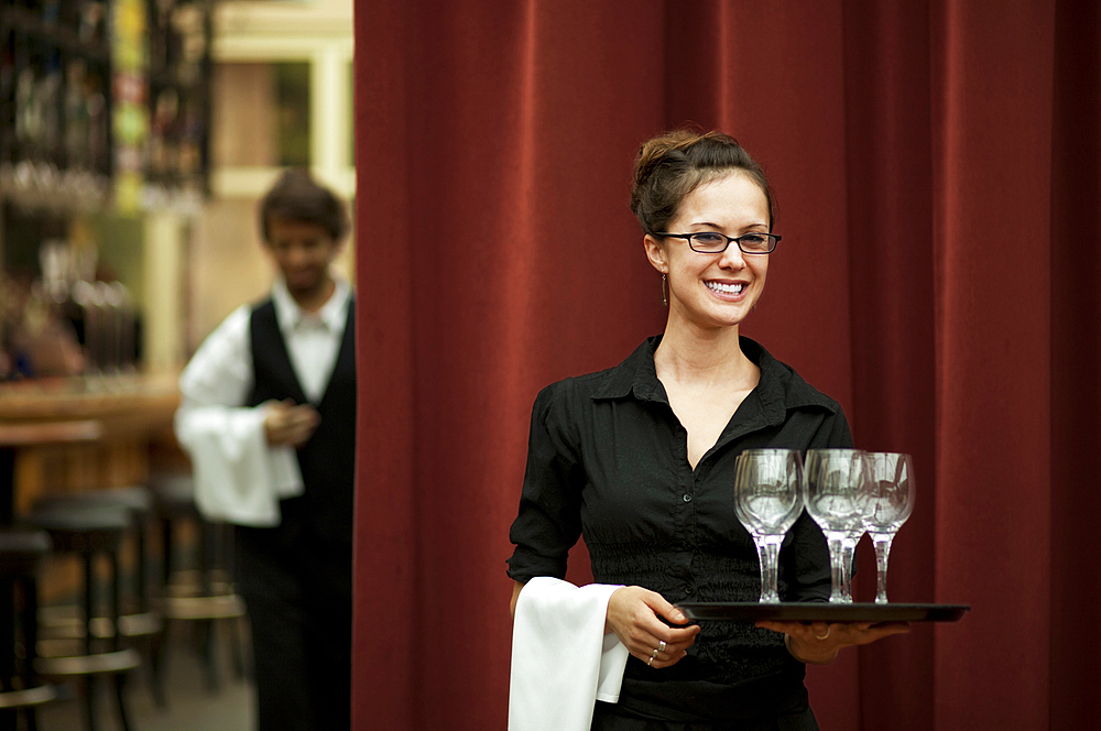 Smiling Hispanic waitress carrying tray of wine glasses