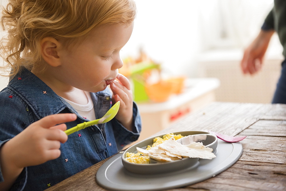 Caucasian girl eating with fingers and spoon