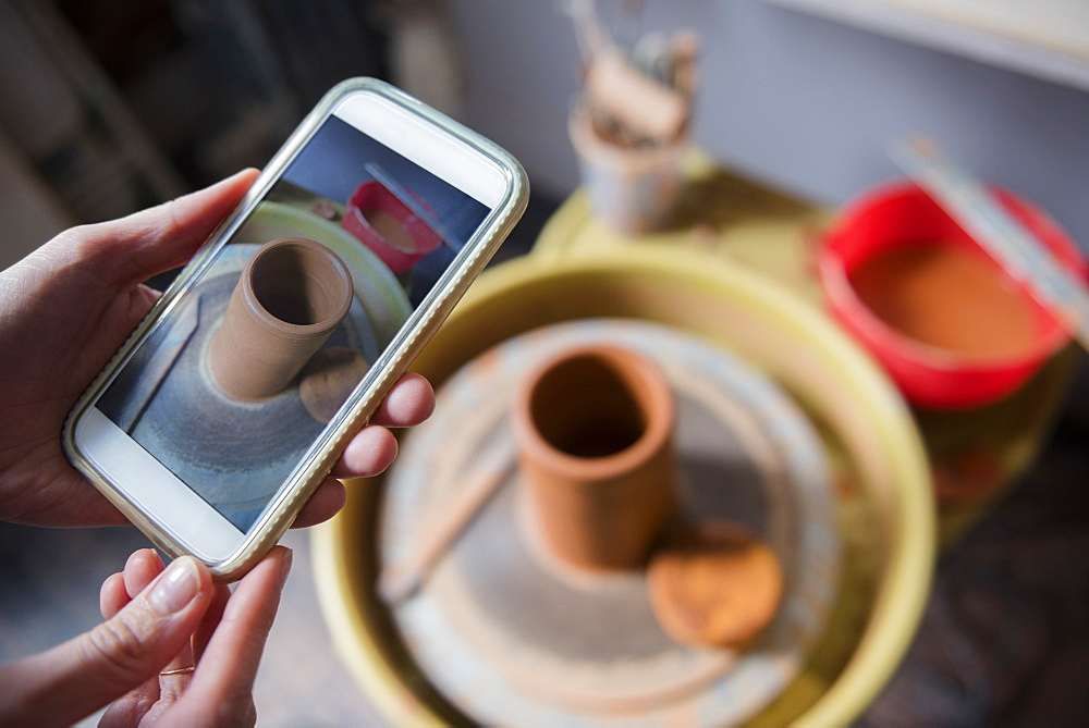 Hands of Caucasian woman photographing pottery with cell phone