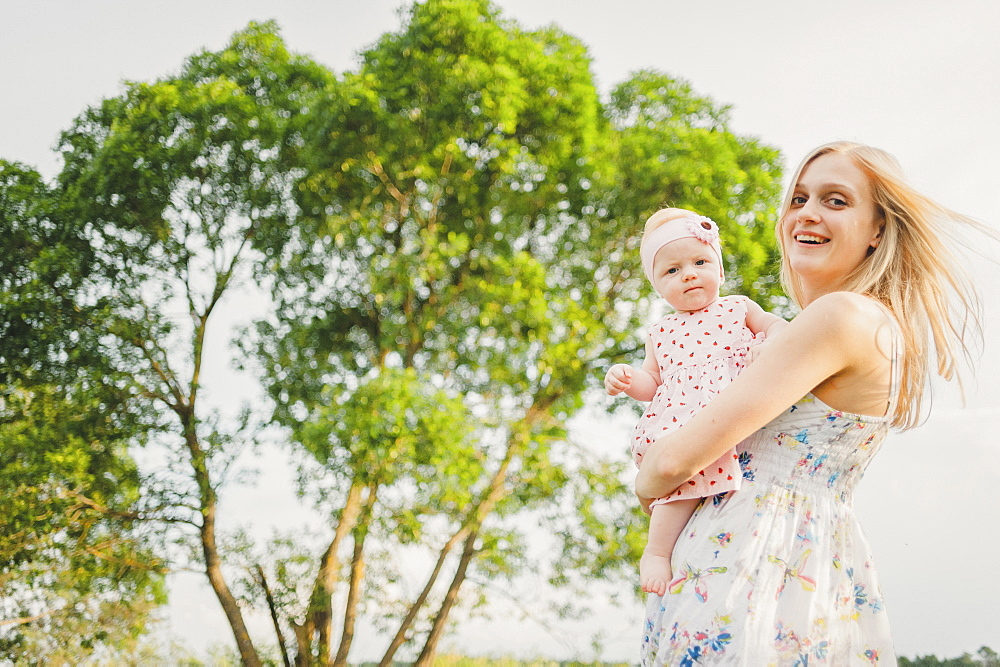 Mother carrying baby daughter near tree