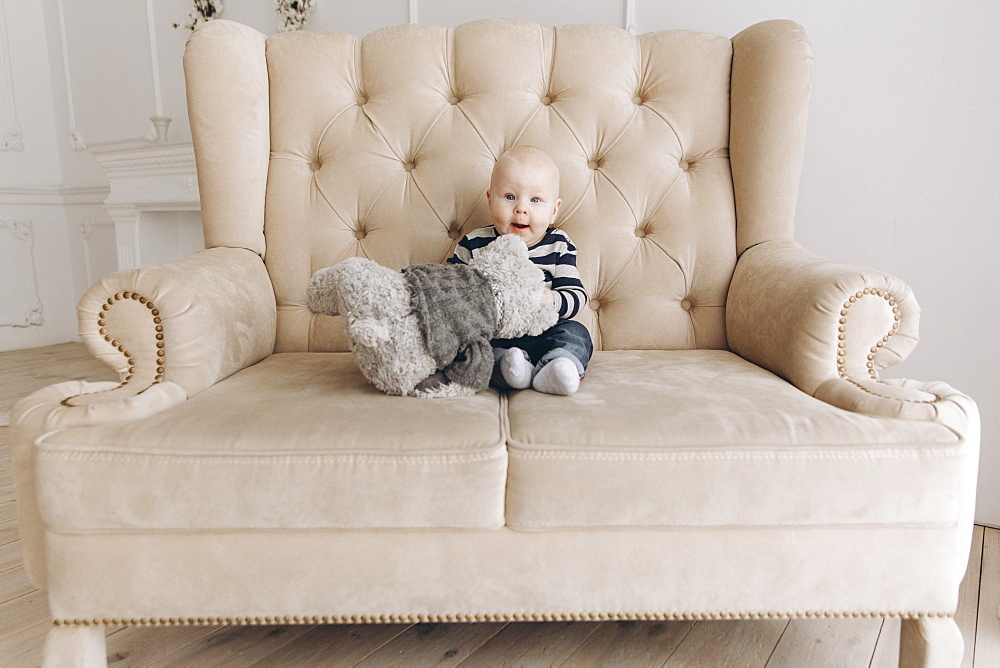 Caucasian baby boy sitting on love seat playing with teddy bear