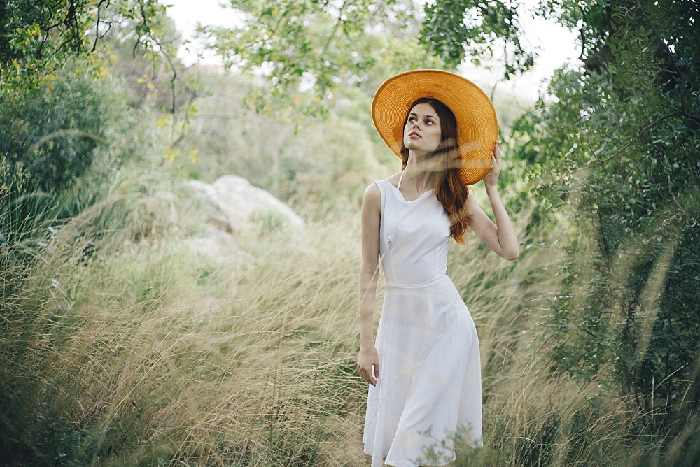 Caucasian woman wearing hat walking in tall grass