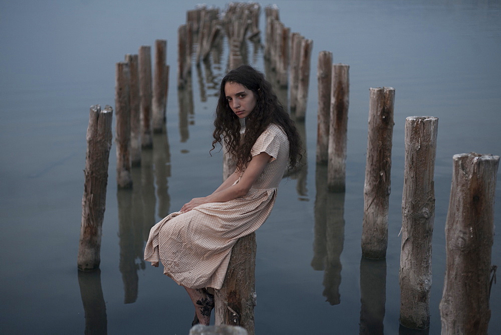 Serious Caucasian woman sitting on piling in river