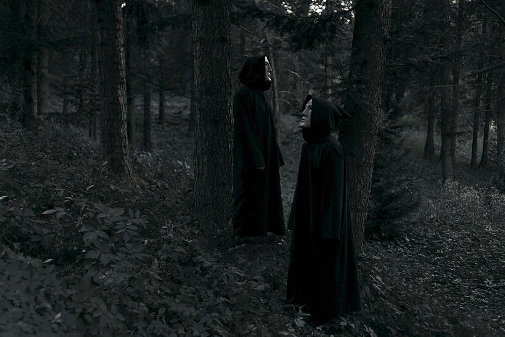 People wearing black robes and white masks standing in forest