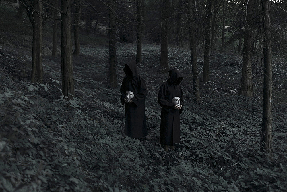 People wearing black robes and holding white masks in forest