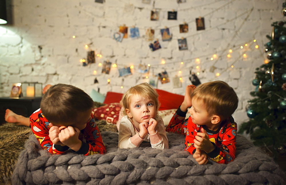 Caucasian girls and boy laying on bed near Christmas tree