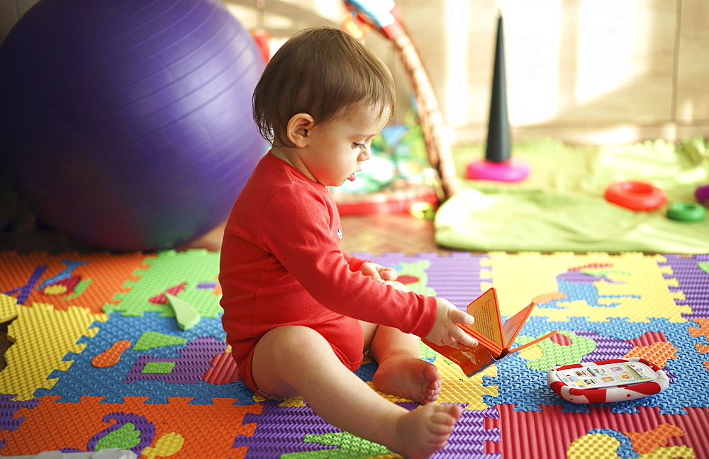 Baby boy sitting on playroom floor holding book