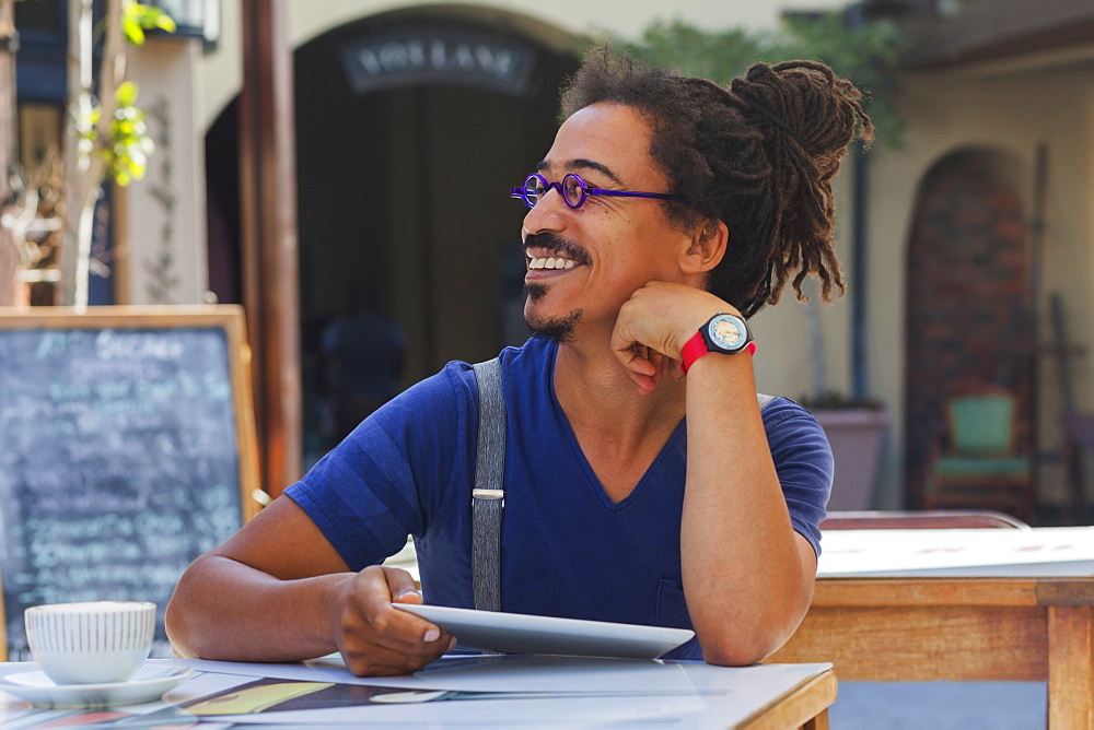 Smiling mixed race man using digital tablet at sidewalk cafe