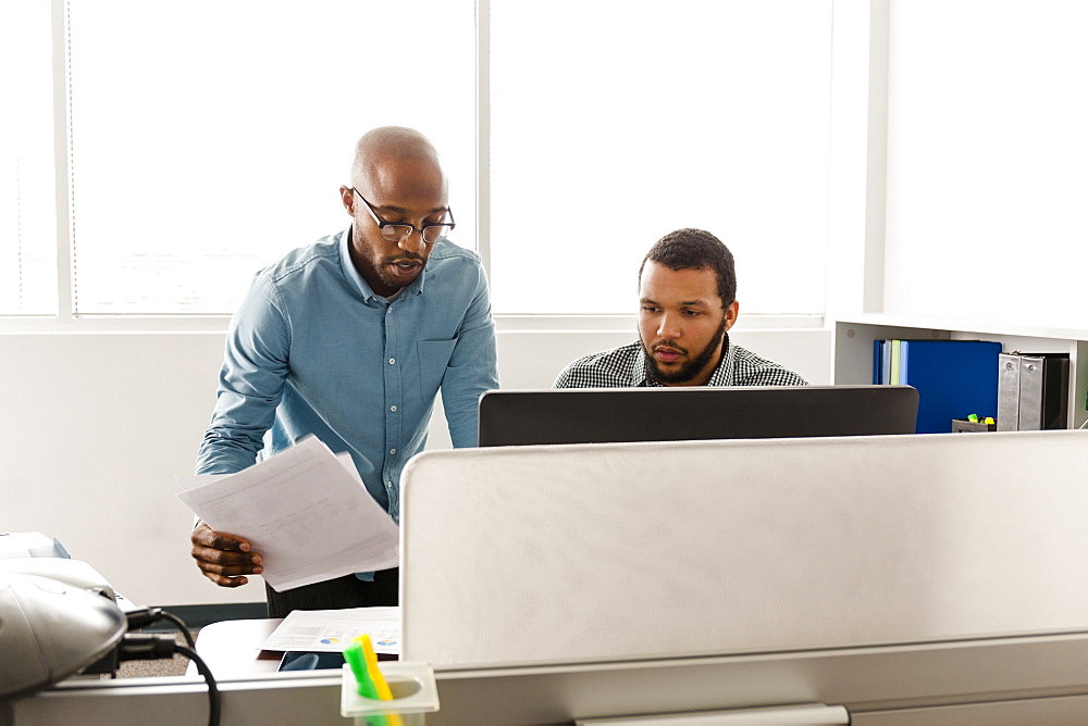 Men working at computer with paperwork in office