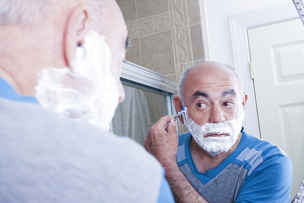 Reflection of Hispanic man shaving face in mirror