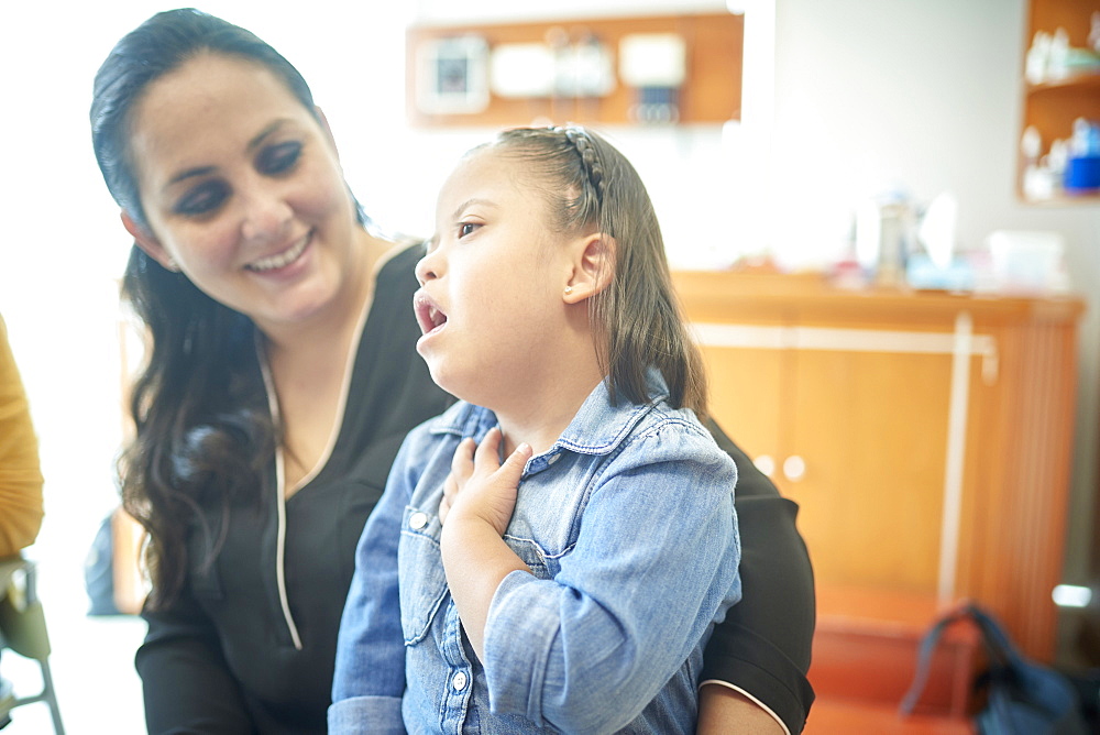 Hispanic mother watching daughter with Down Syndrome pointing to neck