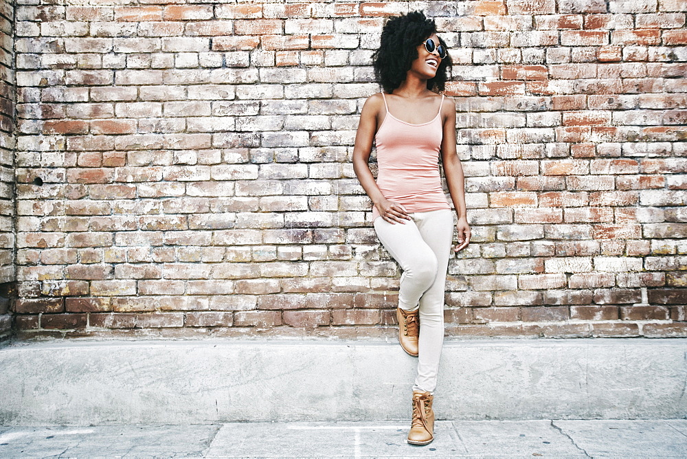 Laughing Black woman leaning on brick wall