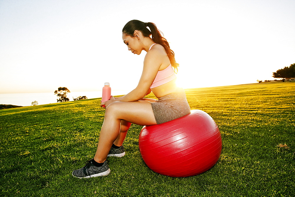 Mixed Race woman resting on fitness ball in sunny field