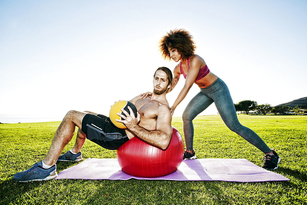 Couple exercising with fitness ball and heavy ball in sunny field