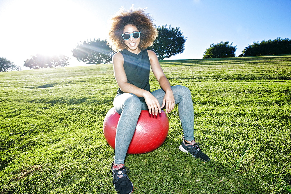 Portrait of smiling Hispanic woman sitting on fitness ball in field