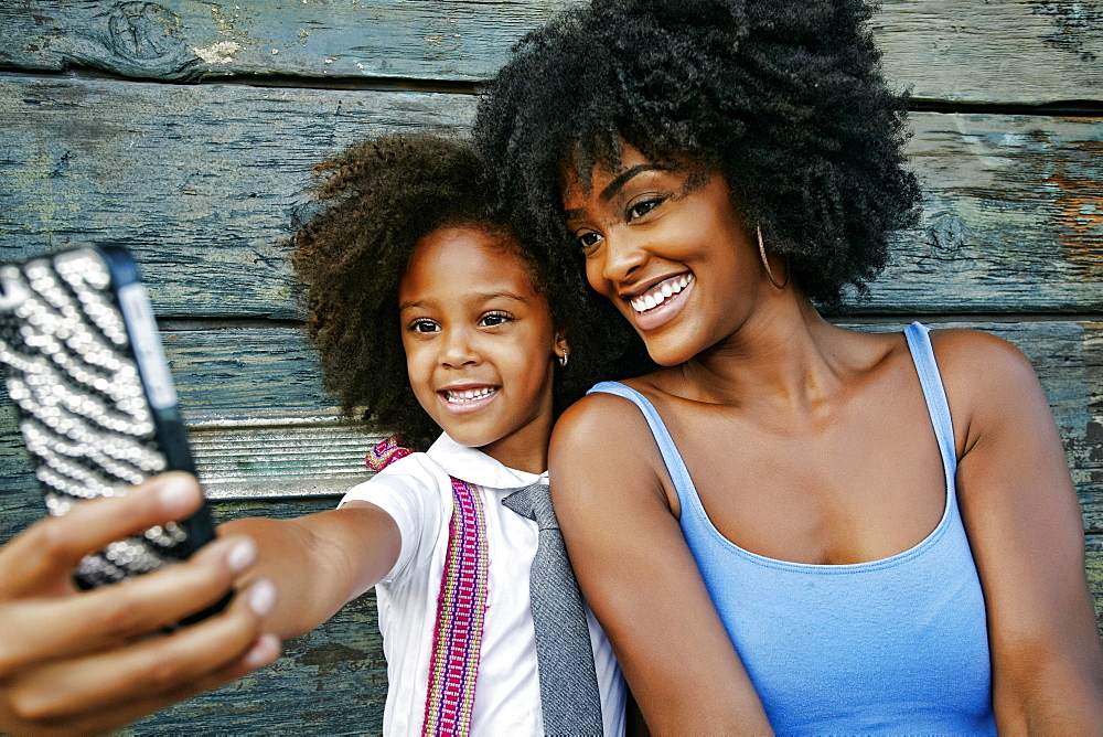 Smiling mother and daughter posing for cell phone selfie