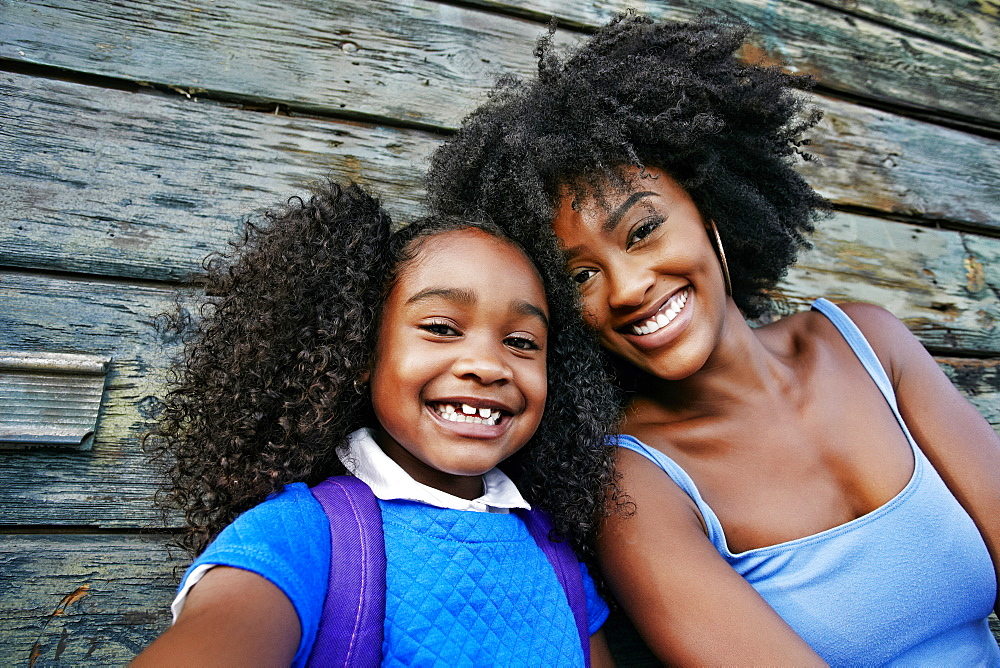 Portrait of smiling Black mother and daughter near wooden wall