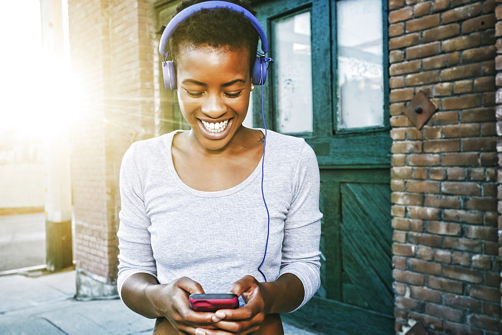 Smiling Black woman listening to cell phone with headphones in city