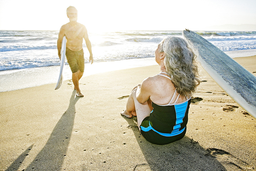 Older Caucasian couple on beach with surfboards