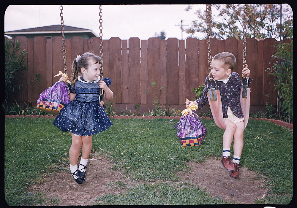 Caucasian brother and sister on swings holding Easter baskets