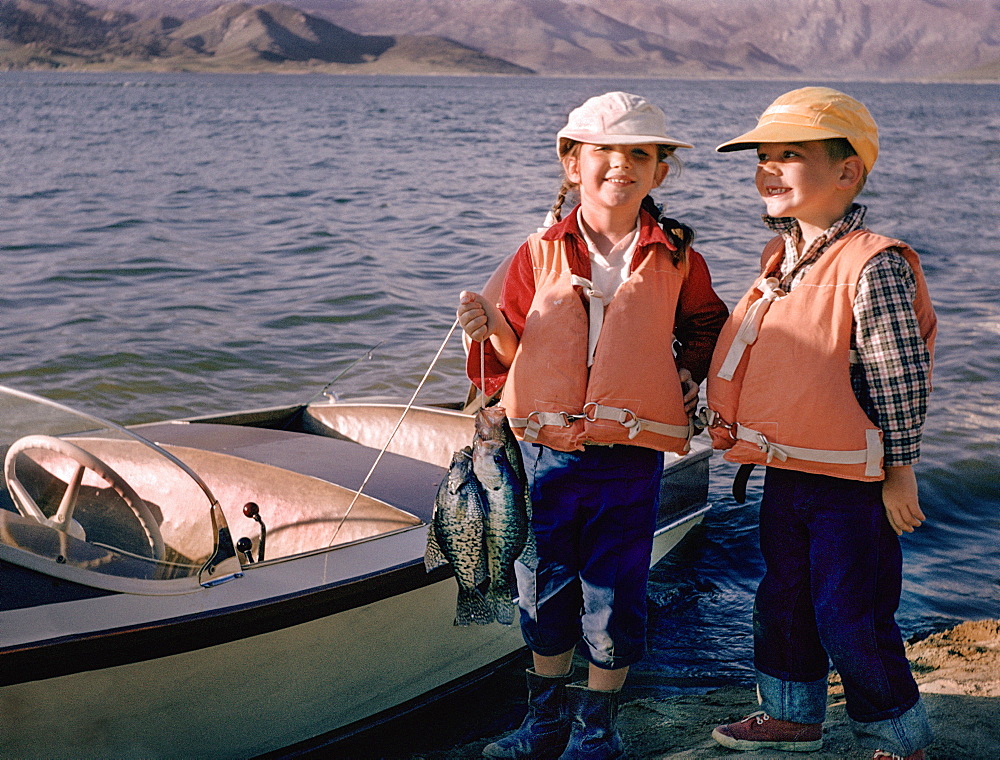 Portrait of Caucasian brother and sister posing with fish near boat