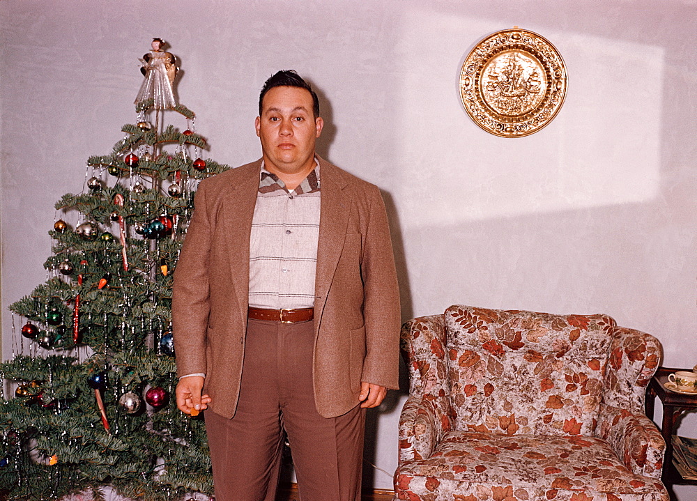 Serious Caucasian man posing near Christmas tree