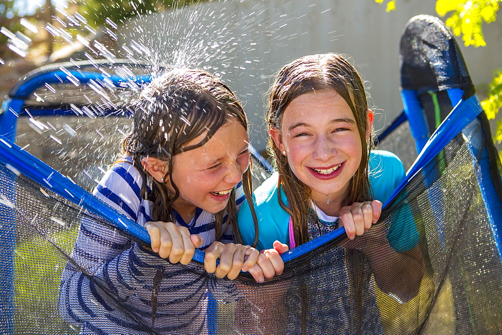 Water splashing on Caucasian girls leaning on netting