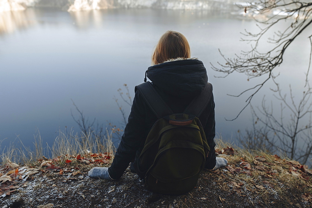 Caucasian woman sitting at the edge of reservoir wearing backpack