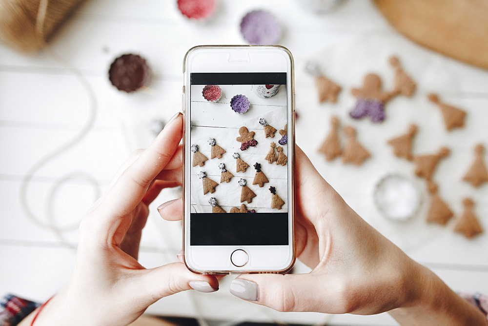 Hands of Caucasian woman photographing Christmas cookies with cell phone