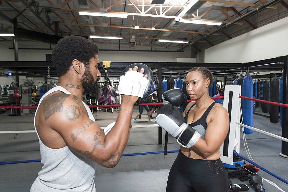 Black woman sparring with trainer in boxing ring