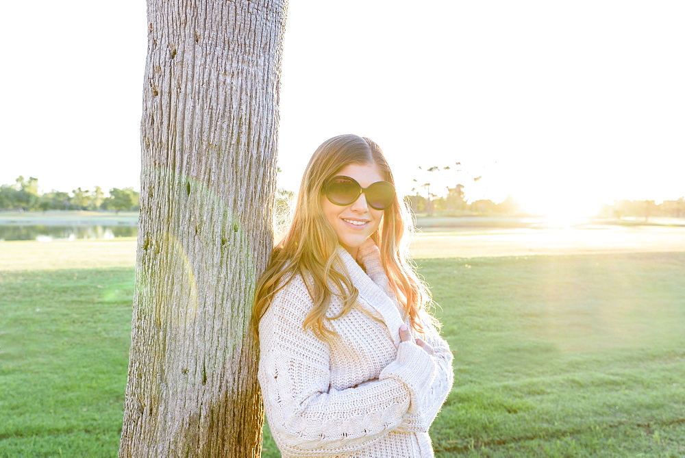 Portrait of smiling Hispanic woman wearing sunglasses leaning on tree