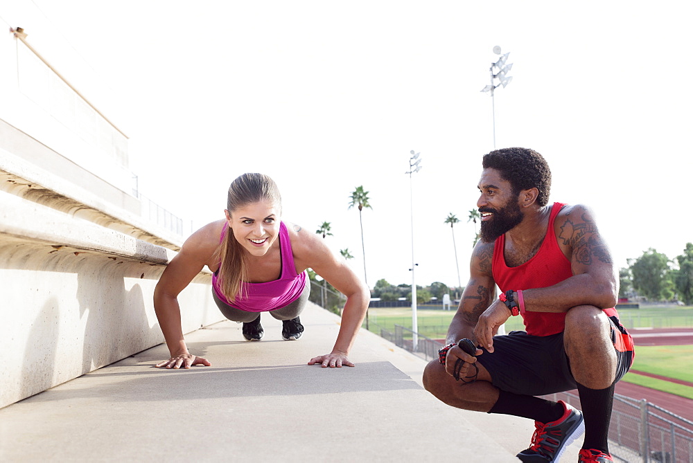 Trainer watching woman do push-ups on bleachers