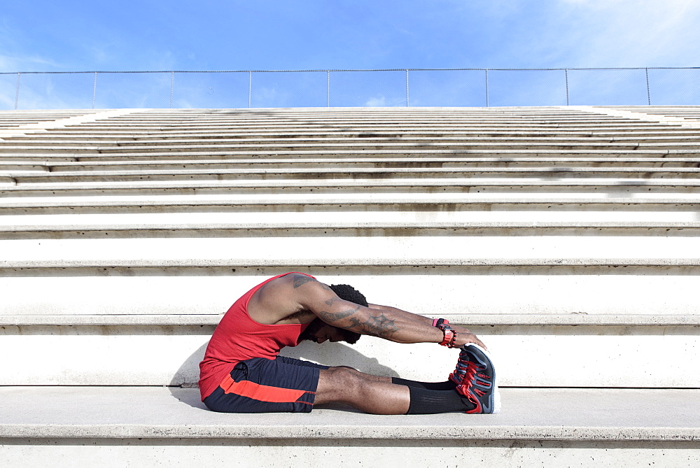 African American man stretching legs on bleachers