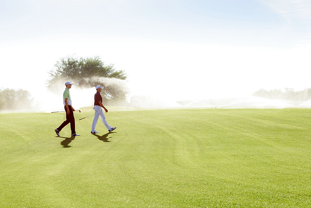 Friends walking on golf course near sprinklers