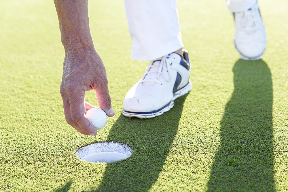 Hispanic man retrieving golf ball from hole on golf course