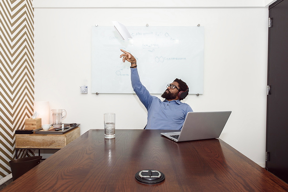 Black businessman wearing headphones throwing paper airplane