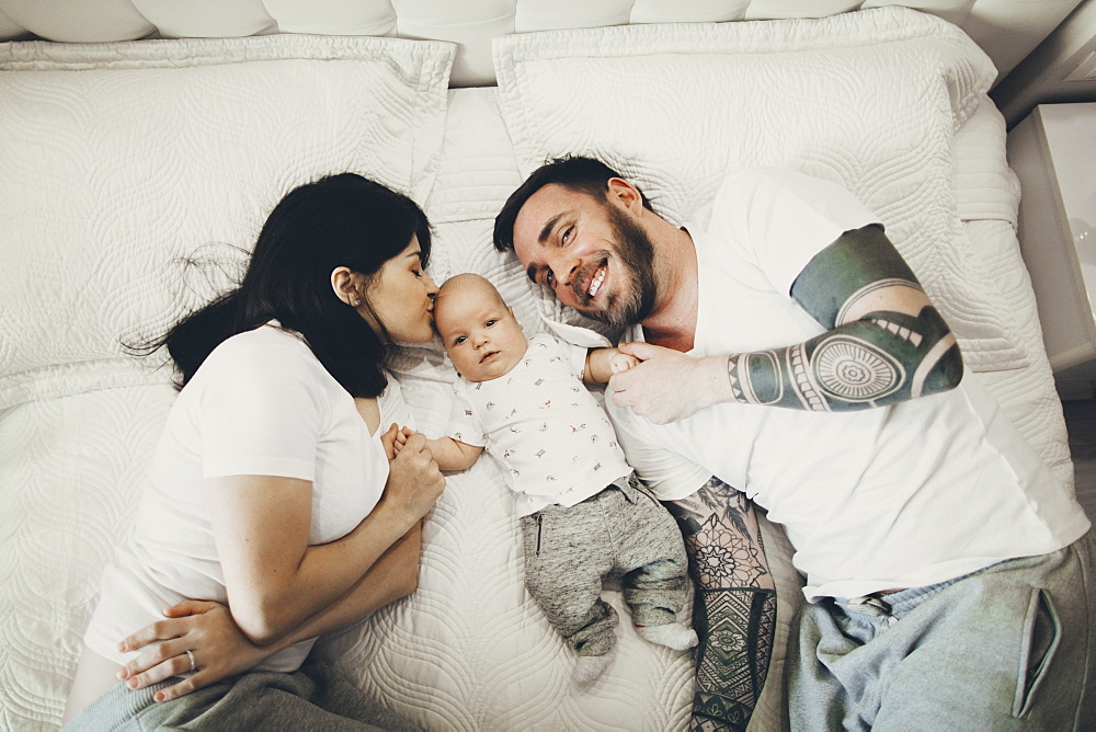 Caucasian mother and father holding hands with baby son on bed