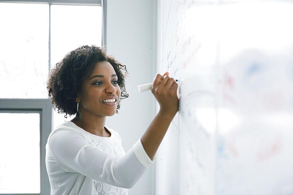 African American businesswoman writing on whiteboard in meeting