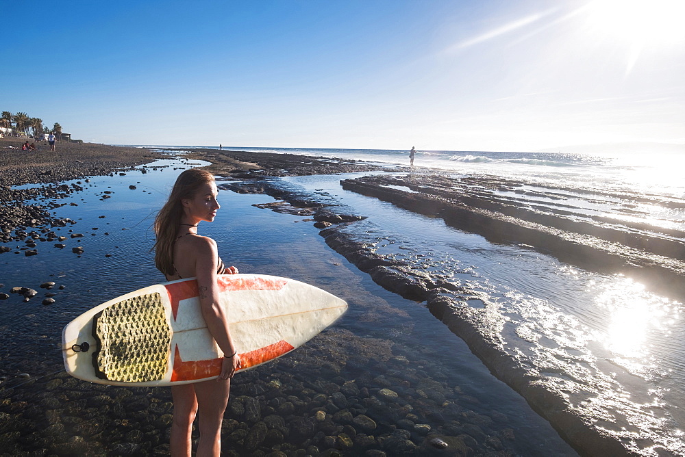 Caucasian woman standing on beach holding surfboard