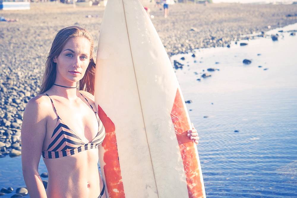 Caucasian woman standing on beach holding surfboard