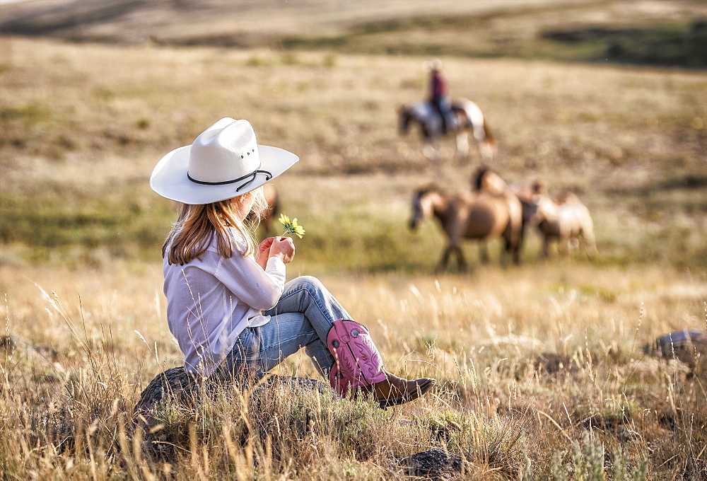 Caucasian girl sitting on rock in field holding flower