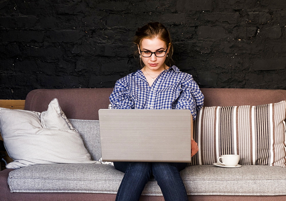 Caucasian woman sitting on sofa using laptop